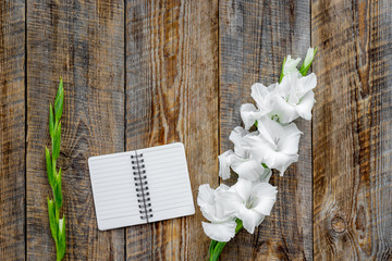 Feminine desk workspace. Notebook and gladiolus on rustic wooden background top view copyspace