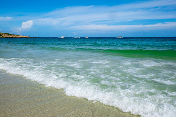 wave of green ocean on sandy beach and blue sky