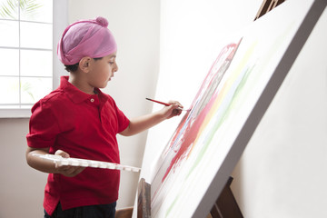 Cute little boy painting on artist's canvas with paintbrush 