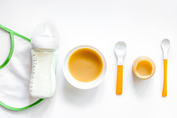 Preparing to feed baby. Puree, spoon, nipple, bottle and bib on white background top view copyspace