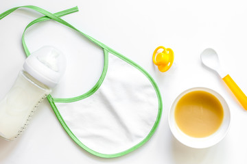 Preparing to feed baby. Puree, spoon, nipple, bottle and bib on white background top view copyspace