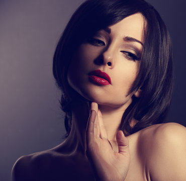 Beautiful makeup sexy woman with short hair style touching her face the hand with hot red on dark shadow background. Art toned portrait. Closeup