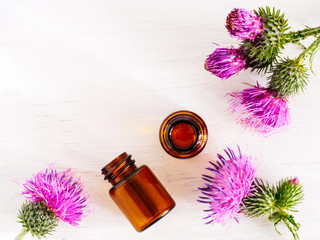 burdock oil in small glass bottle and burdock flowers on white wooden table. Top view or flat lay. Copy space.