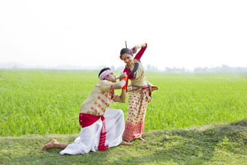 Bihu man blowing on a pepa while Bihu woman dances to his tune 