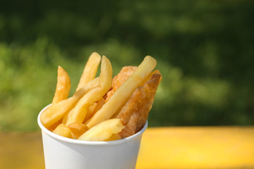 Tasty fried fish and chips in paper cup outdoors