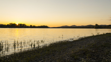 sunset, river view in summer. Colorful landscape summer sunset on the river bank. Sun rays and reflections on water