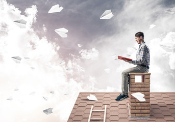 Handsome student guy reading book and paper planes flying in air