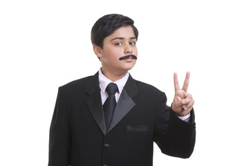 Portrait of boy dressed as businessman giving peace sign