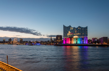 Naklejka premium Hamburg, Germany, Panorama of the Harbour at night. With the colored illuminated music hall at Christopher Street Day
