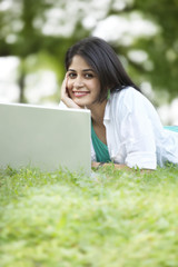 Portrait of young woman using laptop while lying on grass 