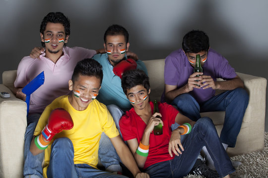 Young male friends watching boxing match together at home 