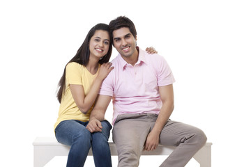 Portrait of a happy young couple sitting on bench over white background 