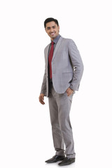 Full length portrait of young businessman with hand in pocket standing against white background 