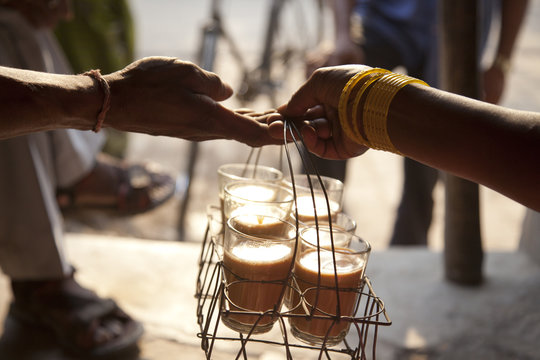 Close-up of female's hand passing tray of chai to man with people in background 