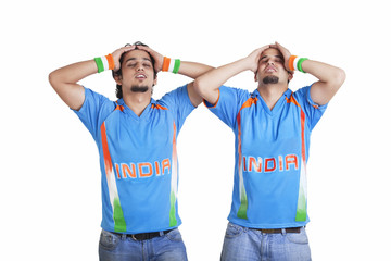 Disappointed young male friends in jerseys standing over white background 