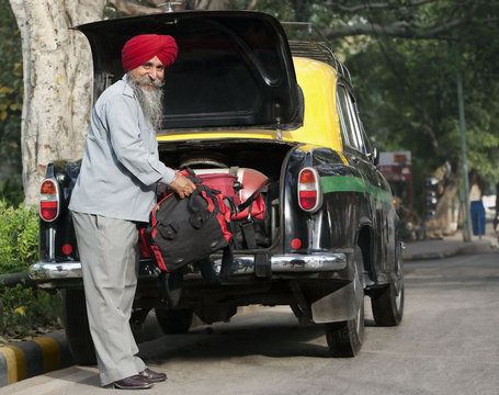 Sikh taxi driver loading luggage into the dickie 