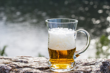 Beer mug stands on a rock above the river