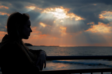 Fototapeta premium female silhouette standing at evening sea coast under light rays, toned image