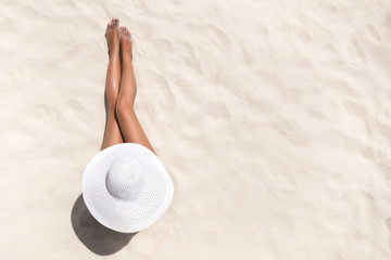 Summer holiday fashion concept - tanning woman wearing sun hat at the beach on a white sand shot from above - Powered by Adobe