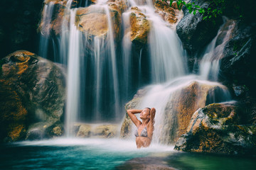 Waterfall woman relaxing in wellness nature water in tropical travel vacation background. Sexy bikini body care girl swimming in natural pool. Health and spa concept.