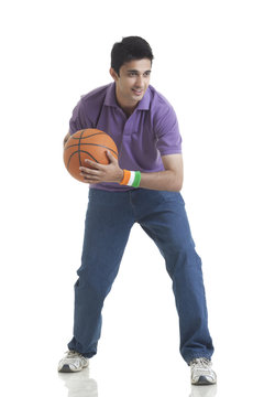 Full length of young man looking away while holding basketball over white background 