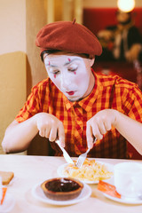 The clown is eating a cake in a cafe and his face is croaking.
