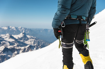 Close up A young guy climber holds in his hand an ice-ax standing on a summit high in the mountains. Extreme sport concept