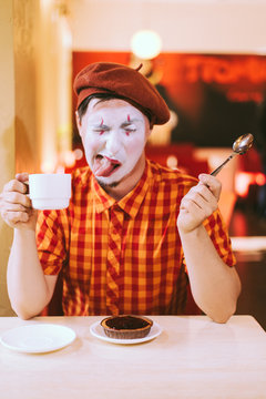 The clown is eating a cake in a cafe and his face is croaking.