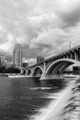 Cloudy morning in Minneapolis. Minneapolis downtown skyline and Third Avenue Bridge above Saint Anthony Falls and Mississippi river in black and white. Midwest USA, state of  Minnesota.