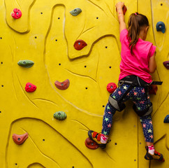 little girl in a pink T-shirt climbing a rock wall indoor