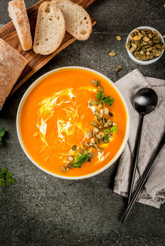 Traditional fall and winter dishes, hot and spicy pumpkin  soup with pumpkin seeds, cream and freshly baked baguette, on black stone table, copy space top view