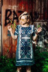 The girl is standing by the wall with cannabis in her hands