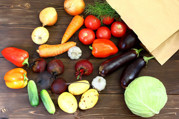 vegetables on wooden background spill out of a paper bag