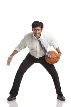 Portrait of smiling young businessman playing basketball 