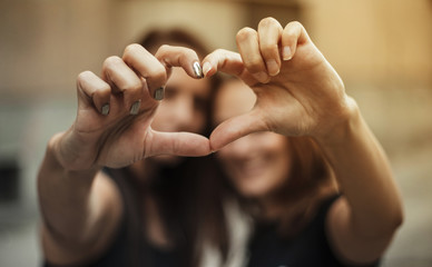 Two female friends making heart with their fingers