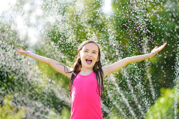 Adorable little girl playing with a sprinkler in a backyard on sunny summer day. Cute child having...