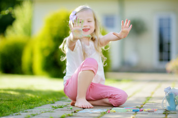 Cute little girl drawing with colorful chalks on a sidewalk. Summer activity for small kids. © MNStudio