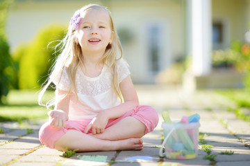 Cute little girl drawing with colorful chalks on a sidewalk. Summer activity for small kids. © MNStudio