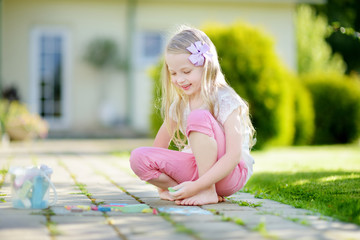 Cute little girl drawing with colorful chalks on a sidewalk. Summer activity for small kids. © MNStudio