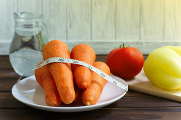 Bunch of carrots wrapped with measuring tape, tomatoes, bell peppers and jug of water on the table. Healthy food, diet, weight loosing and well-being