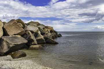 Large rocks on the beach with a cloudy blue sky background