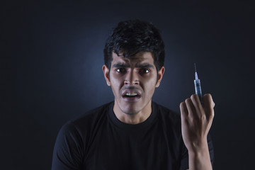 Portrait of confused drug addict with syringe against black background