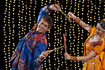 Portrait of young man performing Dandiya Rass with woman against neon lights