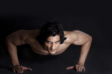 Fototapeta na wymiar Portrait of muscular young man stretching against black background 