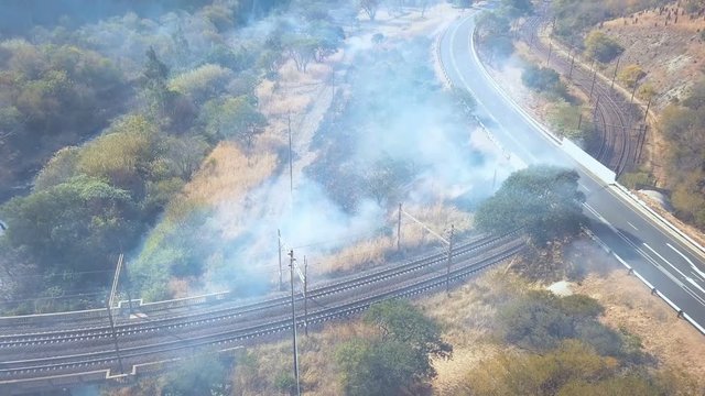 Aerial tilt shot through smole from bush fire on side of road in valley