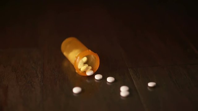 Orange Pill Bottle Falls and Some Pills Fly Out. a prescription orange bottle falls and some white pills fly out of the opening on a wooden surface towards the camera. Slow motion
