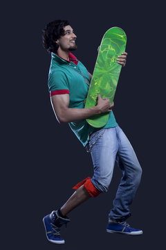 Full length of young man holding a skateboard like a guitar against black background 