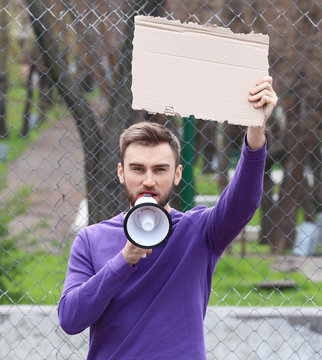 Protesting young man holding piece of cardboard with space for text and megaphone on street