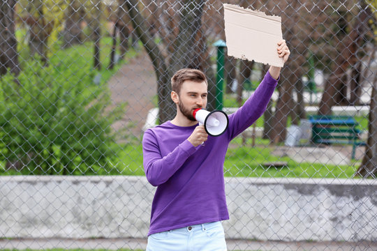 Protesting young man holding piece of cardboard with space for text and megaphone on street