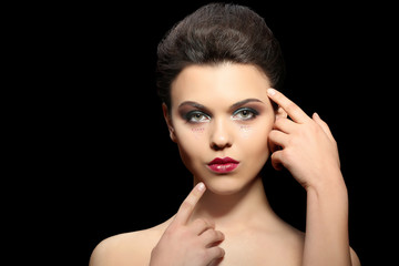 Beautiful young woman with creative makeup on dark background